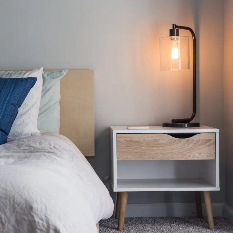 ベッド横のナイトテーブルに置かれた点灯中のモダンなデスクランプ