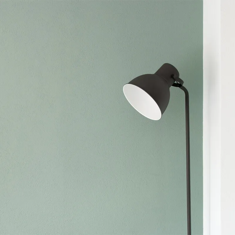 ミントグリーンの壁の前に立つ黒いフロアランプ